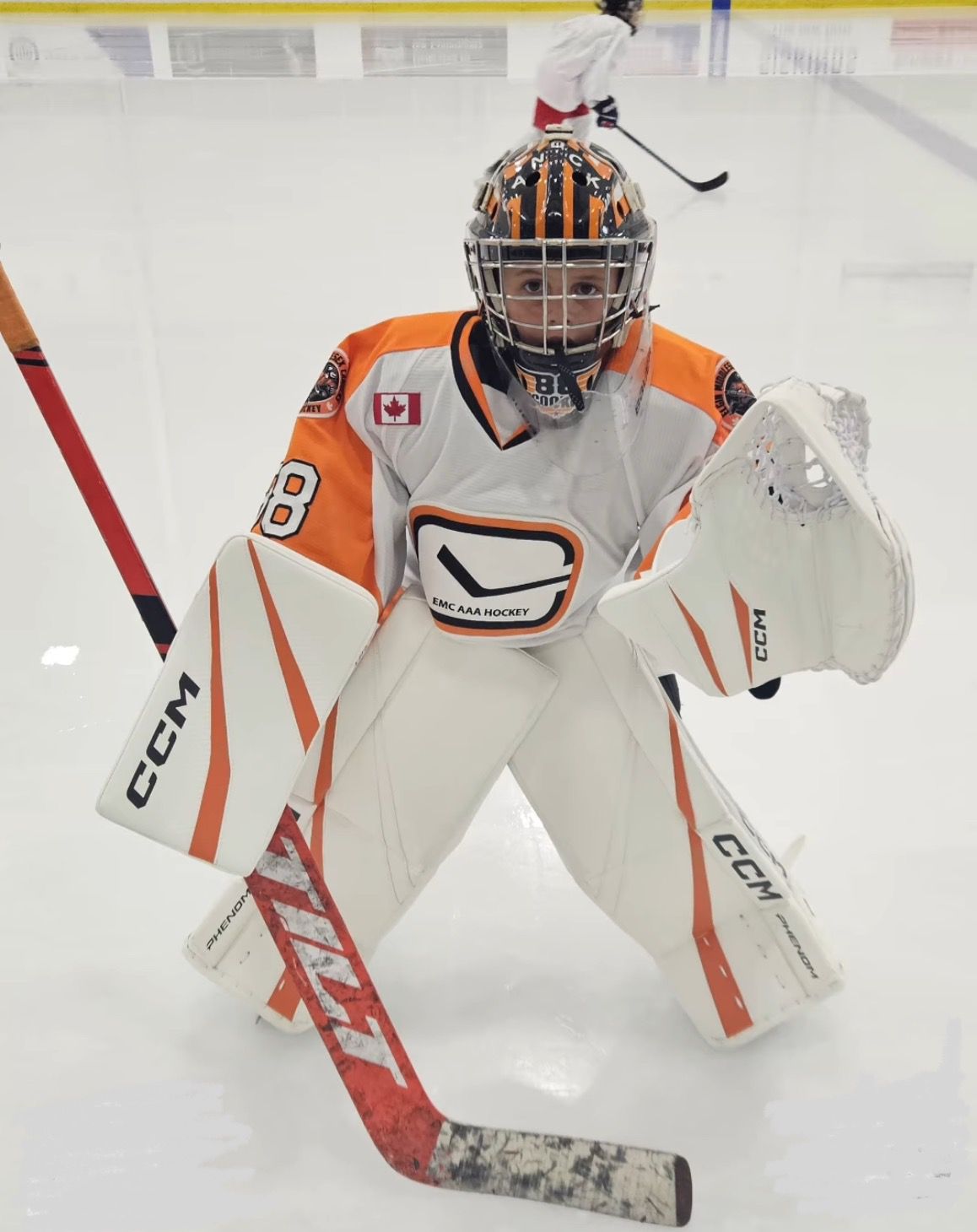EMC AAA goalie in butterfly position with orange Tilt goalie stick