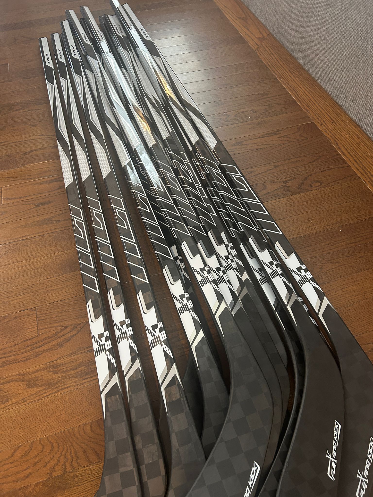 Row of black and white Tilt hockey sticks lined up on hardwood floor