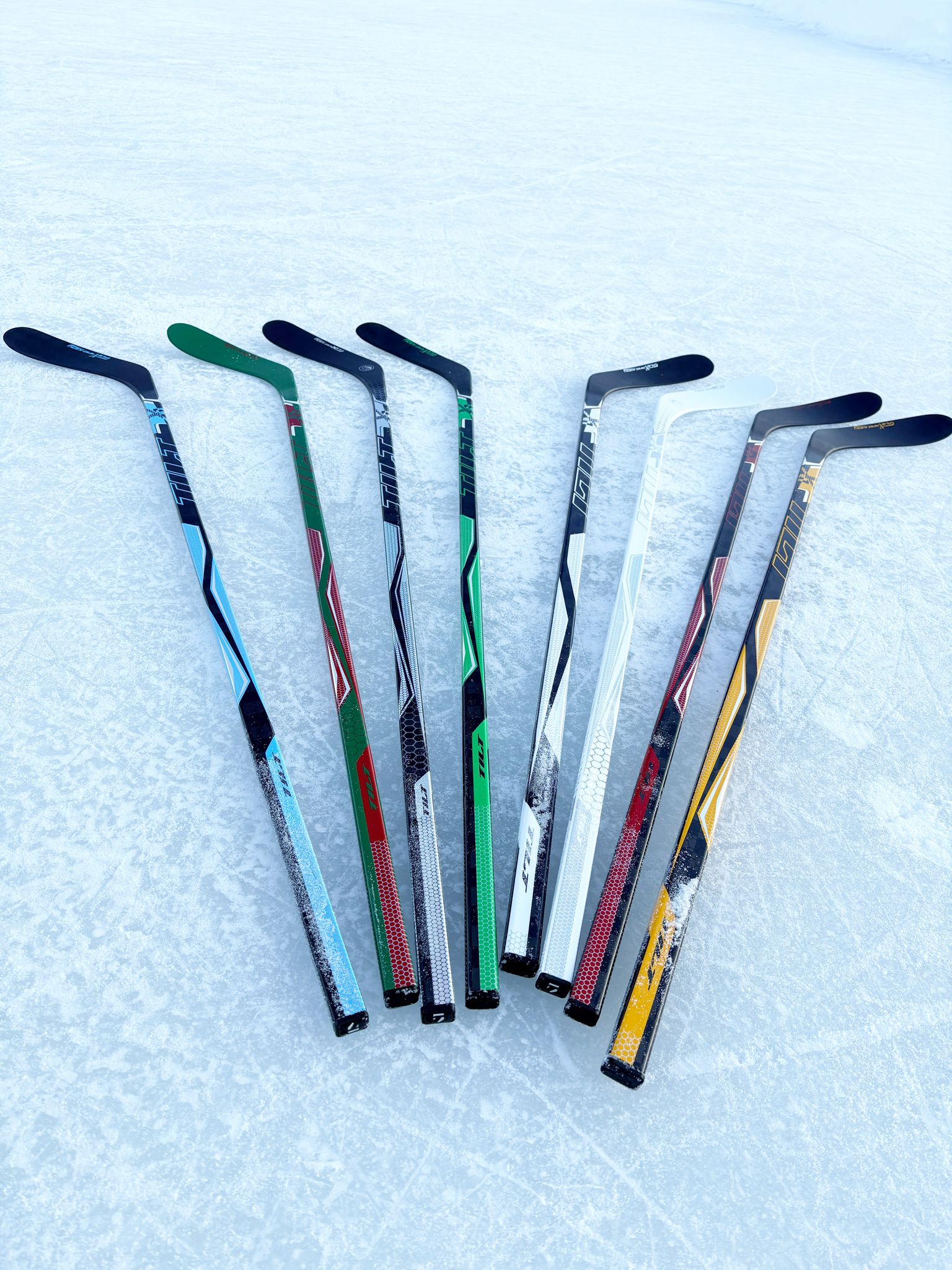 Multiple Tilt hockey sticks fanned out on ice showing various colorways